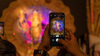 Photographing Goddess Durga idol with phone at puja pandal in Kolkata, West Bengal, India