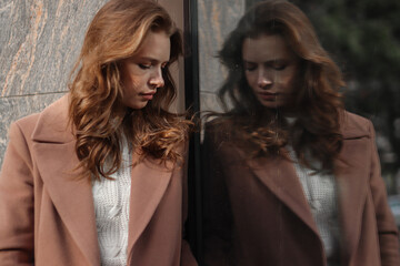 Fototapeta premium Street photo session of a girl with blond long hair in a beige coat. Photo shoot in the big city.