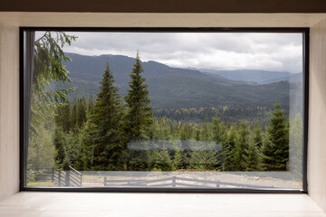 Panoramic window with scenic view on pine forest and mountains