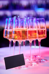 A blank black card with space for text against a Set of glasses with white wine in a nightclub