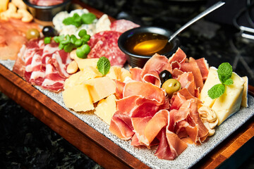 A wooden plate with various Cheese and cut dried deli meats