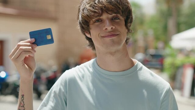 Young blond man smiling confident holding credit card at street