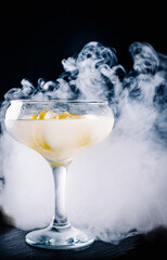 Alcohol gin cocktail in the glass with smoke on dark background.
