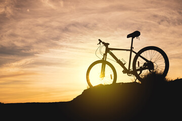 Fototapeta na wymiar silhouette of a bicycle on a hill against the sky during sunset. evening bike ride, the bike is in the grass