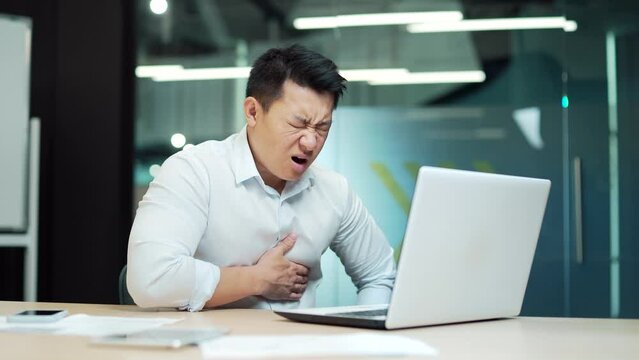 Asian business Man employee with a heart attack office worker with severe heart pain. holding chest . male businessman Sitting at work a computer desk. manager suffers in Workplace. Indoor. Asia