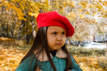 A 4-year-old girl in a red beret pouted her lips and stood dissatisfied. The concept of children's emotions, demanding child.