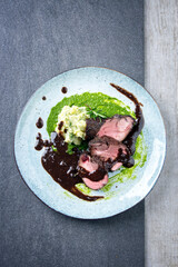 Traditional German venison roast with mashed potatoes, basil pesto and spicy red wine sauce served as top view on a Nordic design plate