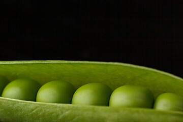 An open green pea pod on a dark background