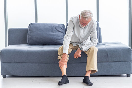 Health care and problem concept Uhappy senior man suffering from knee ache at home. Knee joint injury. Gout. Rheumatoid. Arthritis. Osteoporosis
