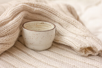 A white ceramic cup wrapped in knitted warm blanket or sweater. Warmth, cozy atmosphere concept.