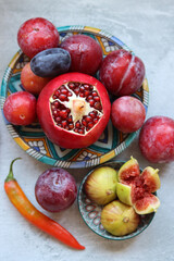 Fresh Mediterranean fruit on a blue ceramic plate. Colorful still life with pomegranate, figs, plums. Healthy eating concept. 