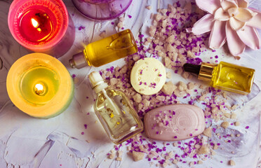 Lavender-scented sea salt crystals scattered on a table, soap bars, bottles of face, body care oil, cosmetic essential serum, burning candles flat lay. Spa beauty day. Beautiful composition top view.
