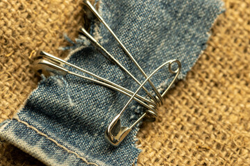 Safety pins on a strip of denim against a homespun fabric with a rough texture.