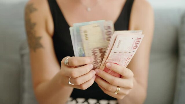 Young woman counting taiwan dollars banknotes at home