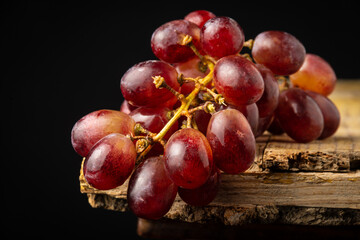 Close-up of bunch of wet black grapes on rustic wooden table, black background, horizontal, with copy space