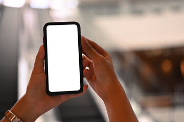 Close up view of hands holding mock up mobile phone with blurred escalator in background