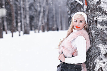 Snowy day blonde girl on a walk in a winter park