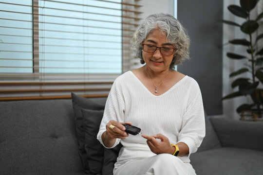 Senior diabetic woman using glucose meter checking blood sugar level at home. Diabetes, health care concept