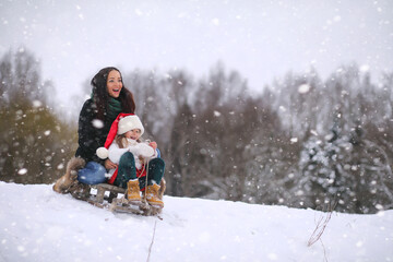 Fototapeta na wymiar A winter fairy tale, a young mother and her daughter ride a sled in the forest. A girl on a sled with gifts on the eve of the new year in the park. 