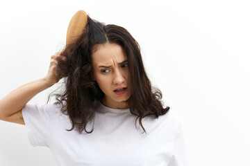 a sad, upset woman tries to comb her long, dark, tangled hair with a wooden massage comb, screaming in pain