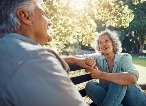 Elderly, couple and happy on bench in garden for conversation, bonding and happiness by trees in summer. Man, woman and retirement show love, relax and smile together in nature with sunshine at park