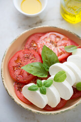 Closeup of sliced mozzarella cheese with red tomatoes and green basil, vertical shot, selective focus