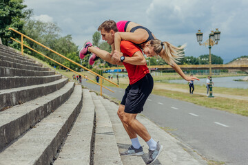 Male athlete carrying his female workout partner on his shoulders while running up the stairs