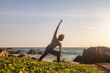 Rear view young woman does asana yoga position on tropical sea coastline beach or ocean, relaxing at sunset. Female performing exercises for healthy lifestyle to restore strength, spirit. Copy space