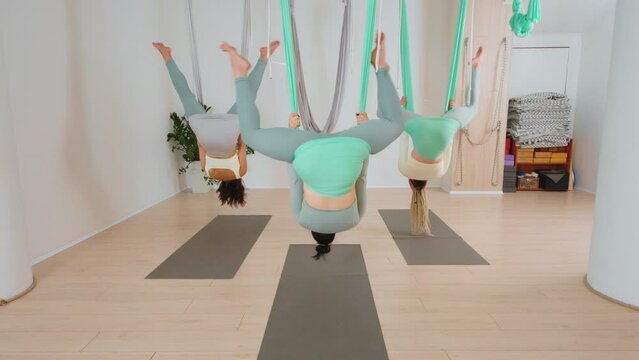 Young fit women doing aerial yoga with a hammock with an instructor in the gym