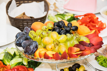 Fruits and vegetables on the festive table. a large glass fruit bowl with plums, peaches, grapes and apricots
