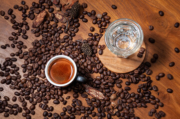 Kawa espresso w czarnej filiżance i szklanka wody  na stole pełnym świeżo palonych ziaren kawy