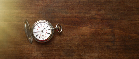 A vintage pocket watch is lying on a wooden table. Mechanical watch with Roman numerals. Round dial...