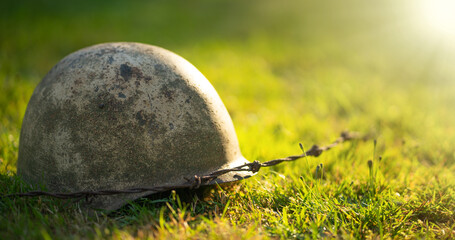 An old soldier's helmet and barbed wire lie on the ground in the rays of the sun. The memory of the...