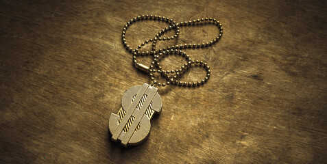 A gold dollar sign on a chain. A gold chain with a dollar symbol on a wooden table.