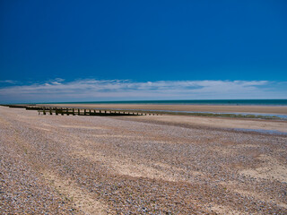 The open expanse of deserted shingle beach at Dungeness, Kent, UK. Taken on a sunny day in summer.