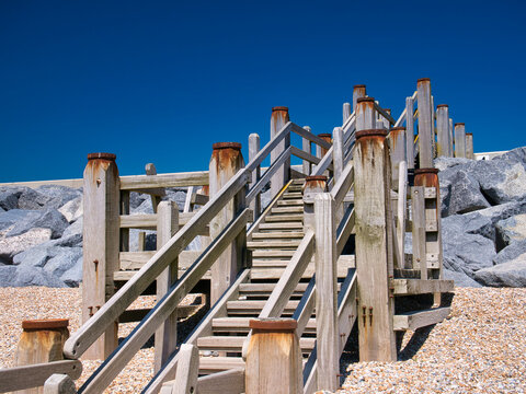Weathered wooden steps give access to the beach at Camber Sands in East Sussex on the south coast of the UK. Taken on a sunny day in summer with a blue sky and no clouds.