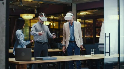 Multi-ethnic office workers testing VR headsets together, using tablet computer and wireless controllers, watching data, working in modern office of hi-tech company. Cyberspace digital technology - Powered by Adobe