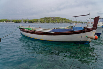 Fototapeta na wymiar White fishing boat for rowing in the beautiful blue crystal clear waters of the Croatian Mediterranean. In the background there is a marina and green mountains.