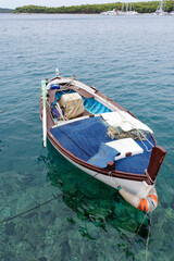 Fototapeta na wymiar Fishing boat, white fishing boat for rowing in the beautiful blue crystal clear waters of the Croatian Mediterranean. In the background there is a marina and green mountains.
