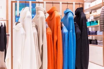 Women's bright knitted jumpers in different colors on hangers in the store. New stylish...
