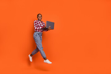 Full body portrait of energetic pretty girl hold netbook jumping isolated on orange color background