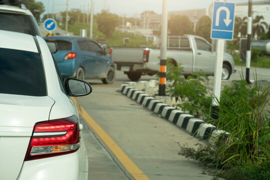 Rear Side Of White Car Stop On The Road And Turn On Right Signal Light For U-Turn. Queuing From Multiple Cars Entering The Expressway. With Green Grass Beside Of The Road.