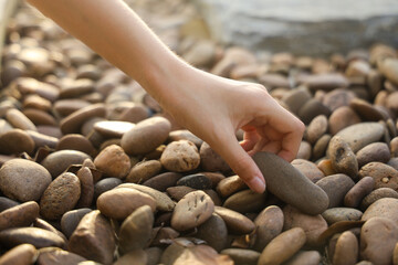 female hand holding small pebble stones picking up pebbles, round shape pebbles, summer vacation souvenir,