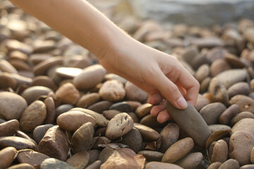 female hand holding small pebble stones picking up pebbles, round shape pebbles, summer vacation...