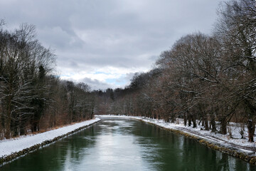 a body of water surrounded by trees isar canal ith snow and Winter sky