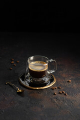 A cup of black coffee in a transparent glass cup on a dark grunge background. Copy space
