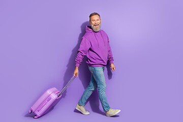 Portrait of retired handsome optimistic man dressed purple hoodie jeans go at airport on plane isolated on violet color background