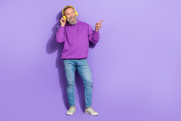 Portrait of positive good mood man wear purple hoodie headphones indicating empty space new release isolated on violet color background