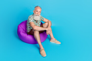 Full size portrait of serious aged person sit comfy bag resting isolated on blue color background