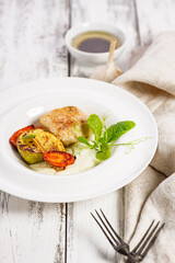 Close-up turkey cutlets and grilled vegetables. Delicious and healthy homemade food. Cheese sauce with garlic and olive oil. Food still life on white wooden background. Vertical shot. Copy space